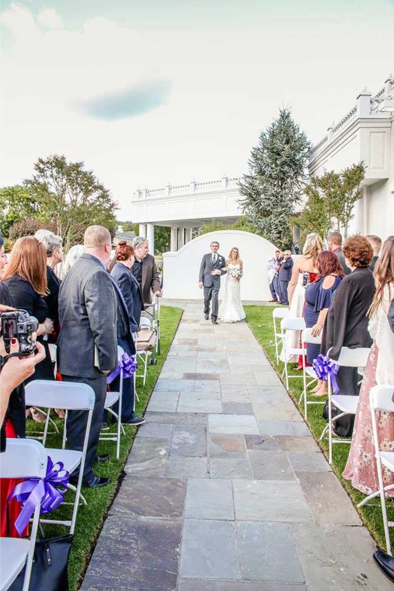 bride-walking-down-stone-aisle-outdoor-wedding-ceremony-with-guests